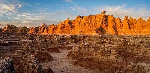 Eroded spires and fluted ridges of pale clay and banded rock rising above a dry drainage at Golden Glow Canyon in Badlands National Park.