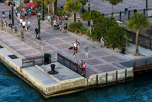 An elevated view over the south corner of Mallory Square in Key West to the concrete seawall and the water beyond, with a street performer in the square