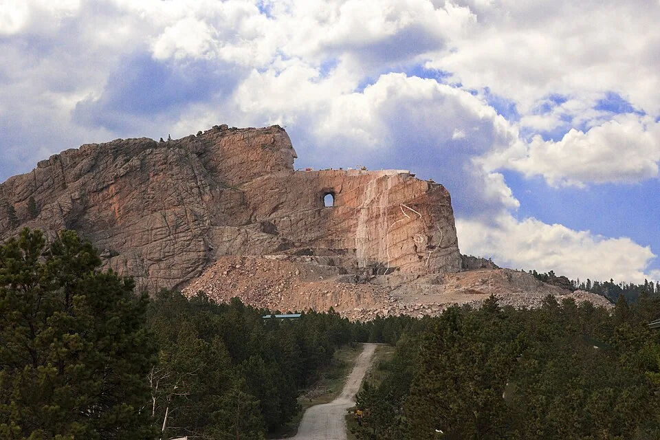 The carved head of Crazy Horse and the roughed-out arm above the tree line, seen from the visitor complex parking area.