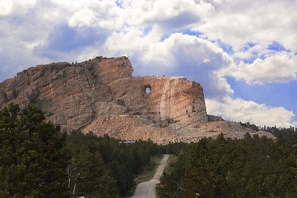The carved head of Crazy Horse and the roughed-out arm above the tree line, seen from the visitor complex parking area.