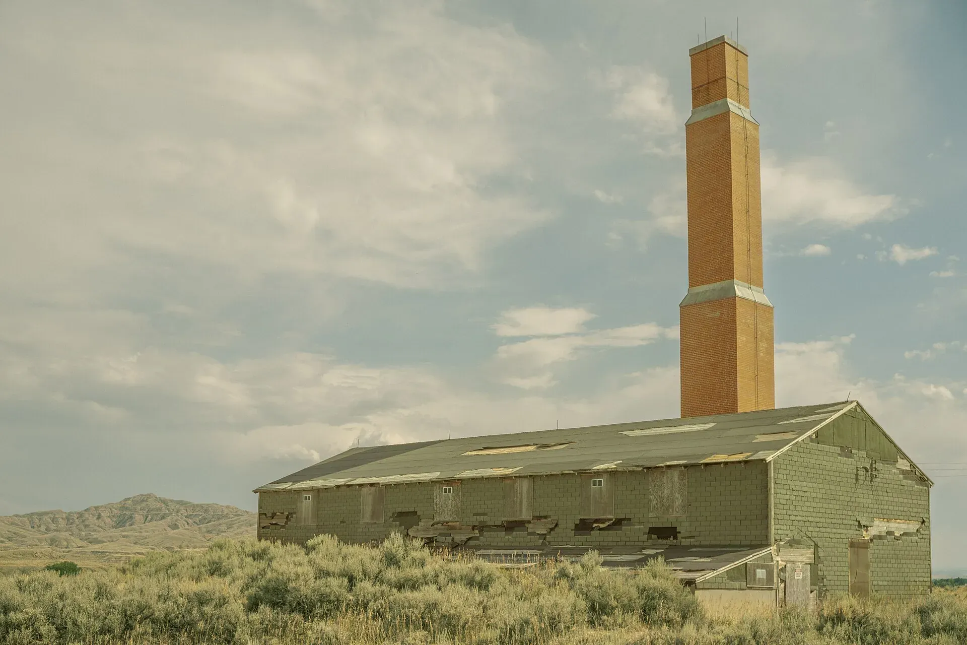 The surviving Heart Mountain hospital buildings with a tall red brick chimney rising above them, sagebrush in the foreground.