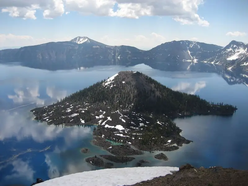 A green, cone-shaped island rising out of the deep blue lake near the caldera wall.