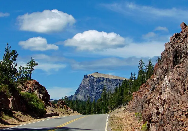 A paved road curving along the rim high above the deep blue lake, with rocky slopes on one side.