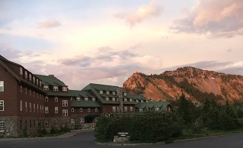 A large stone and wood lodge with a steep roof, standing on the rim above Crater Lake.