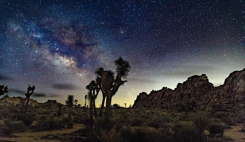 The Milky Way as a bright band of stars stretching across a very dark night sky over open land.