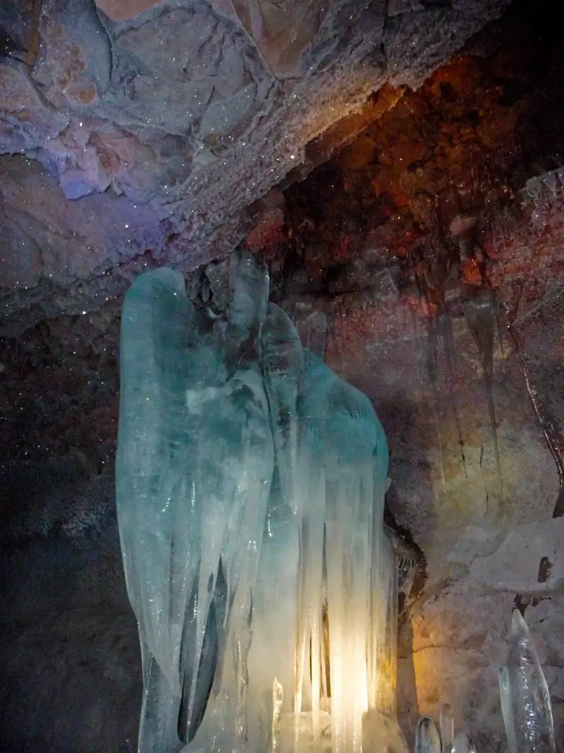 A frozen ice formation inside a dark cave, lit up in blue and green like a waterfall turned to ice.