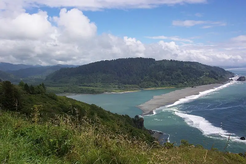 The Klamath River winding through green land to where it meets the blue Pacific Ocean.