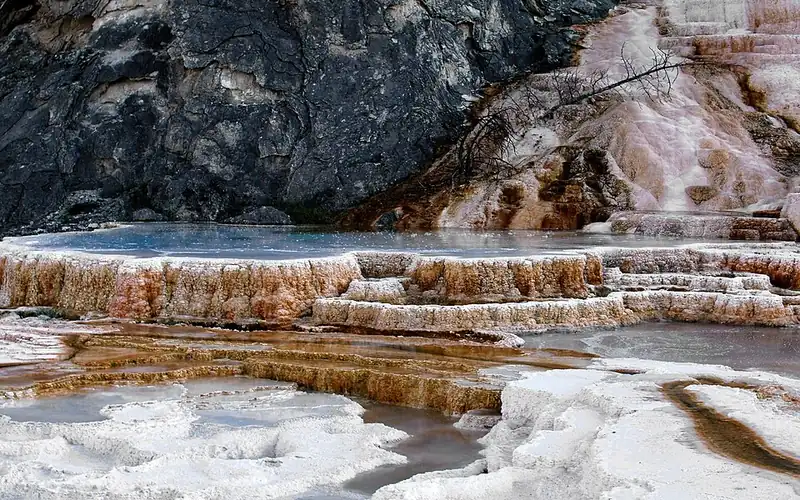 White and orange travertine terraces at Mammoth Hot Springs, with shallow water pooled on the flat steps.