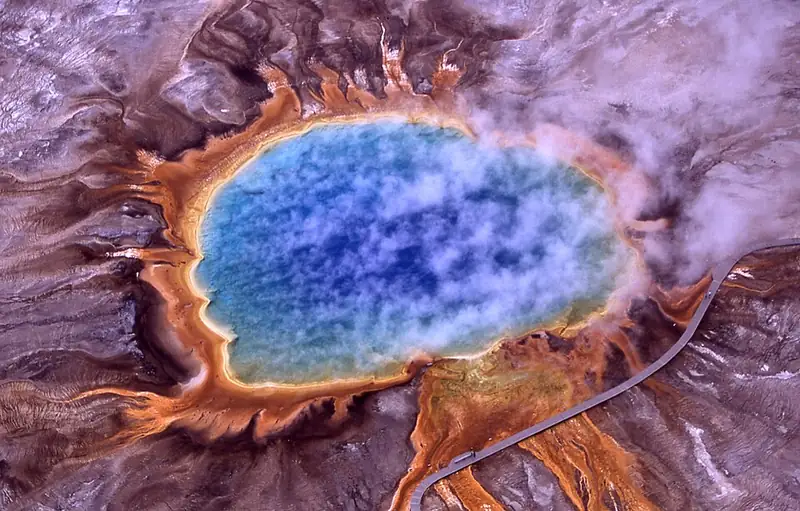 Grand Prismatic Spring seen from above, a deep blue pool ringed by bands of orange, yellow, and brown.