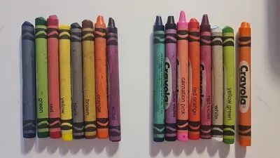 Sixteen Crayola crayons laid out in a row, paper wrappers facing up.