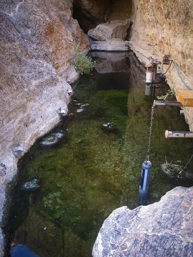 The blue-green water of Devils Hole inside a narrow desert cavern with pale rock walls.